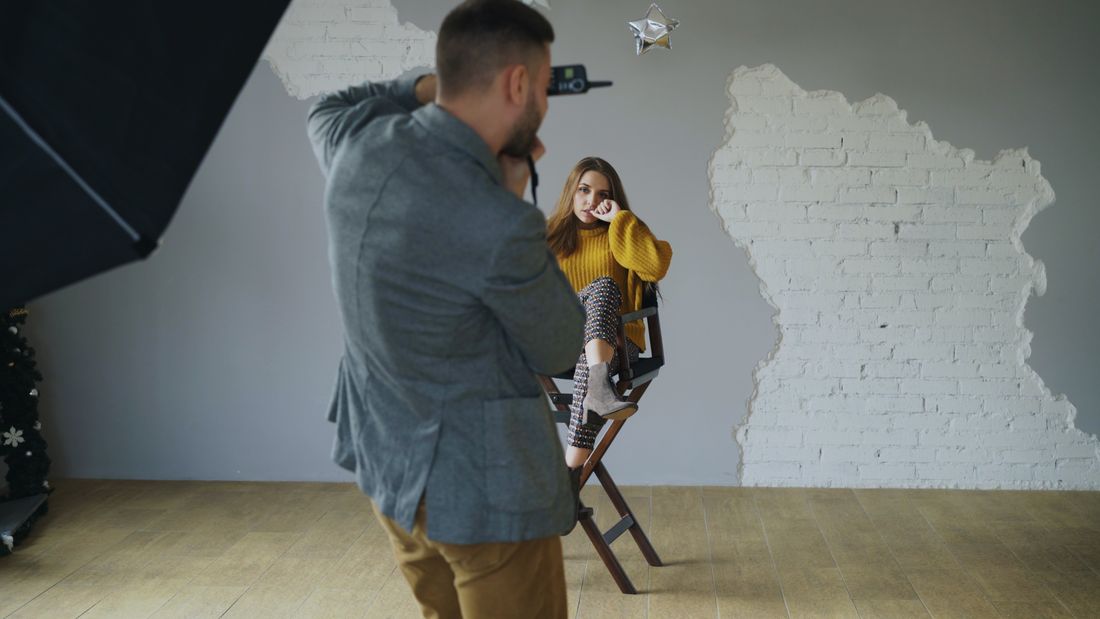 Фотограф знімає білявку-модель у жовтому светрі на високому стільці в студії